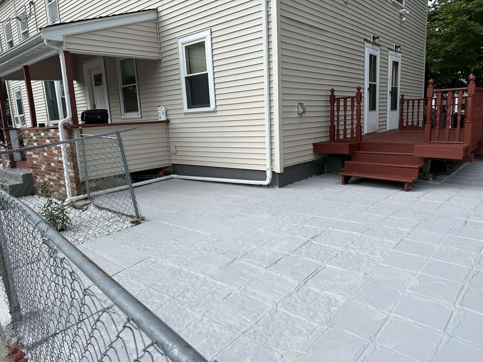 A white house with a red deck and stairs is behind a chain link fence.