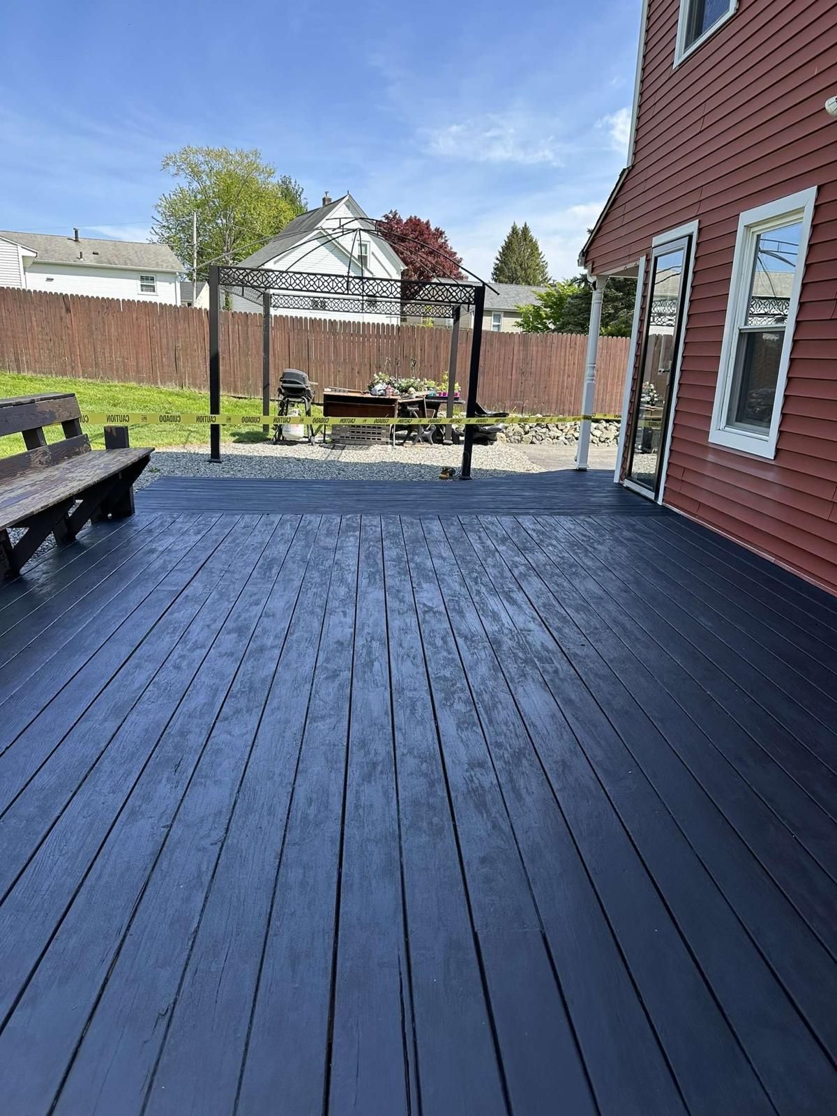 A black deck with a bench and a gazebo in the backyard of a house.