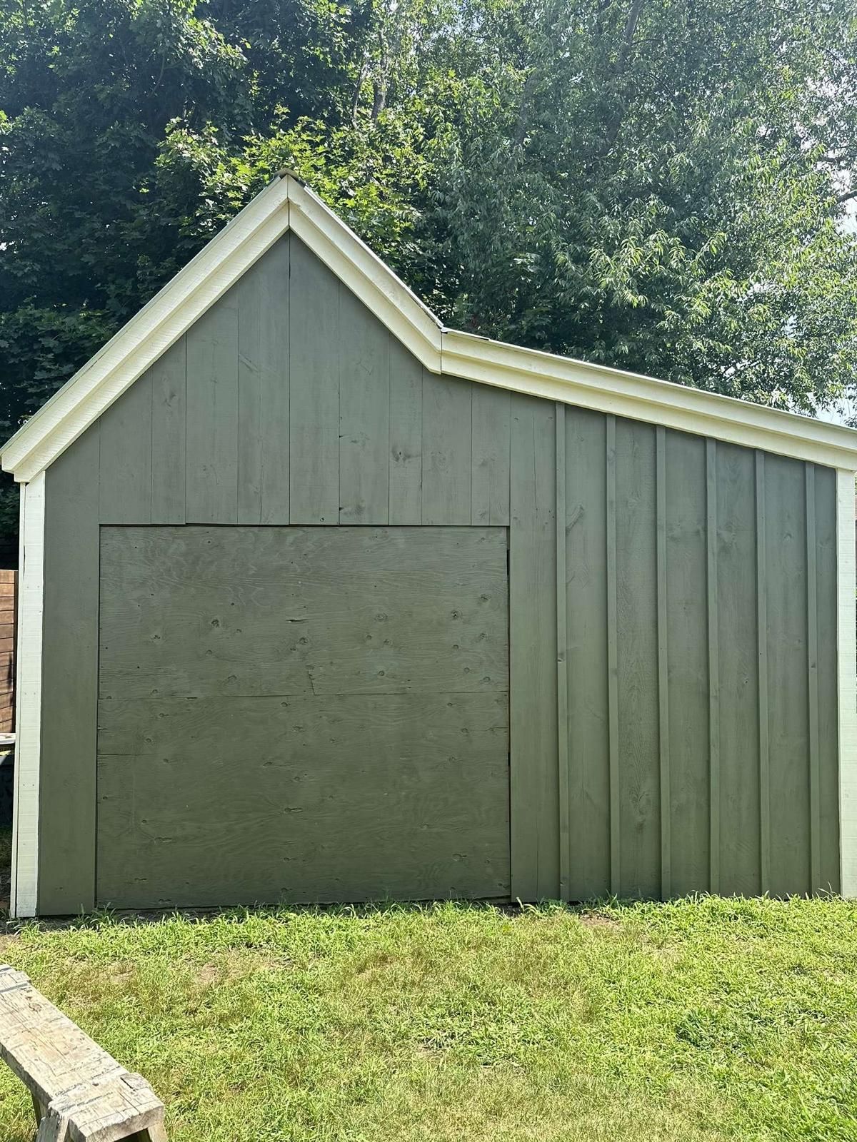 A gray shed with a white roof is sitting in the grass.