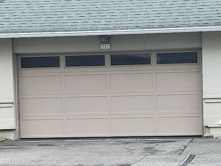 A beige garage door is sitting in front of a white house.