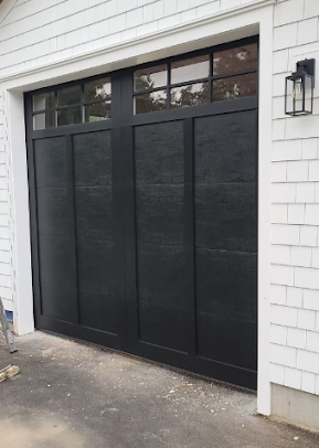 A black garage door is on a white house.