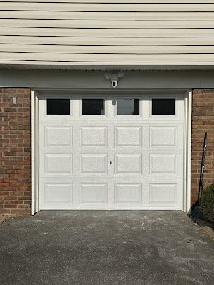 A white garage door is sitting in front of a brick house.