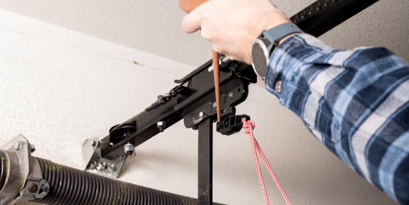 A man is fixing a garage door spring with a wrench.
