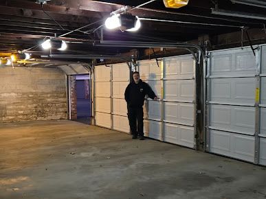 A man is standing in a garage with two garage doors open.