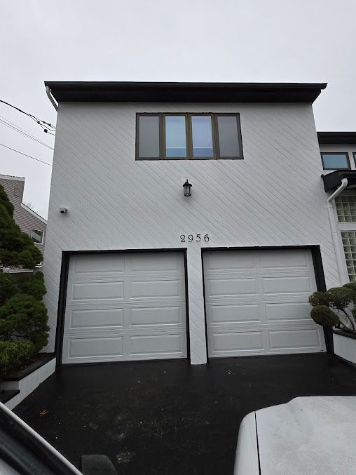 A white house with two garage doors and a car parked in front of it.