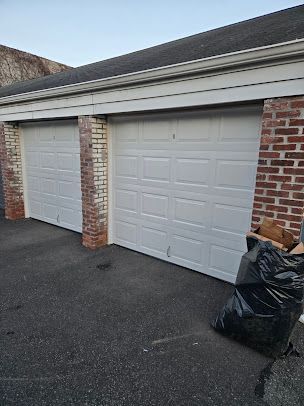 A row of white garage doors next to a brick building.