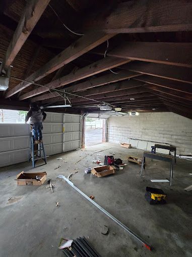 A man is standing on a ladder in a garage working on a garage door.