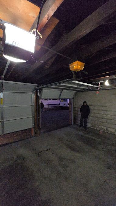 A man is standing in a garage with the door open.