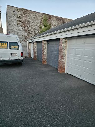 A white van is parked in front of a row of garage doors.