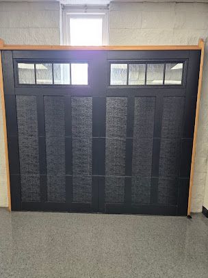A black garage door is sitting in a room next to a window.