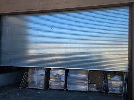 A warehouse with lots of boxes stacked on pallets under a metal shutter.
