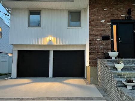 The front of a house with two black garage doors and a brick wall.