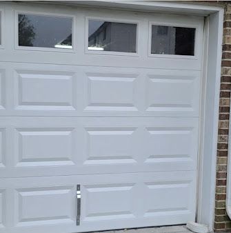 A white garage door with three windows on a brick wall.