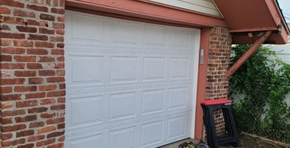 A white garage door is sitting next to a brick wall.