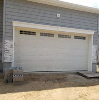 A white garage door is sitting in front of a gray house.