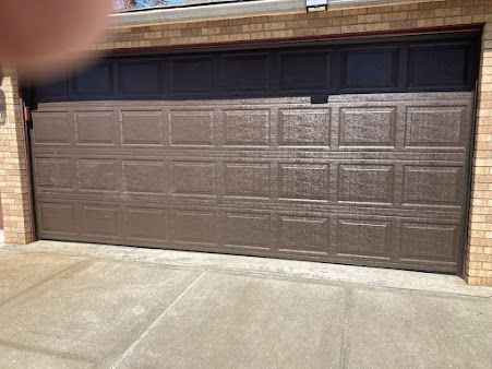 A brown garage door is sitting in front of a brick building.
