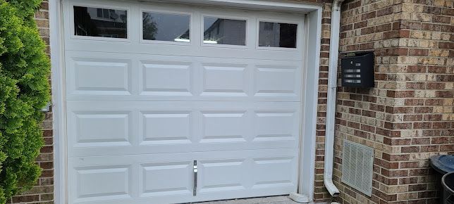 A white garage door is sitting in front of a brick building.