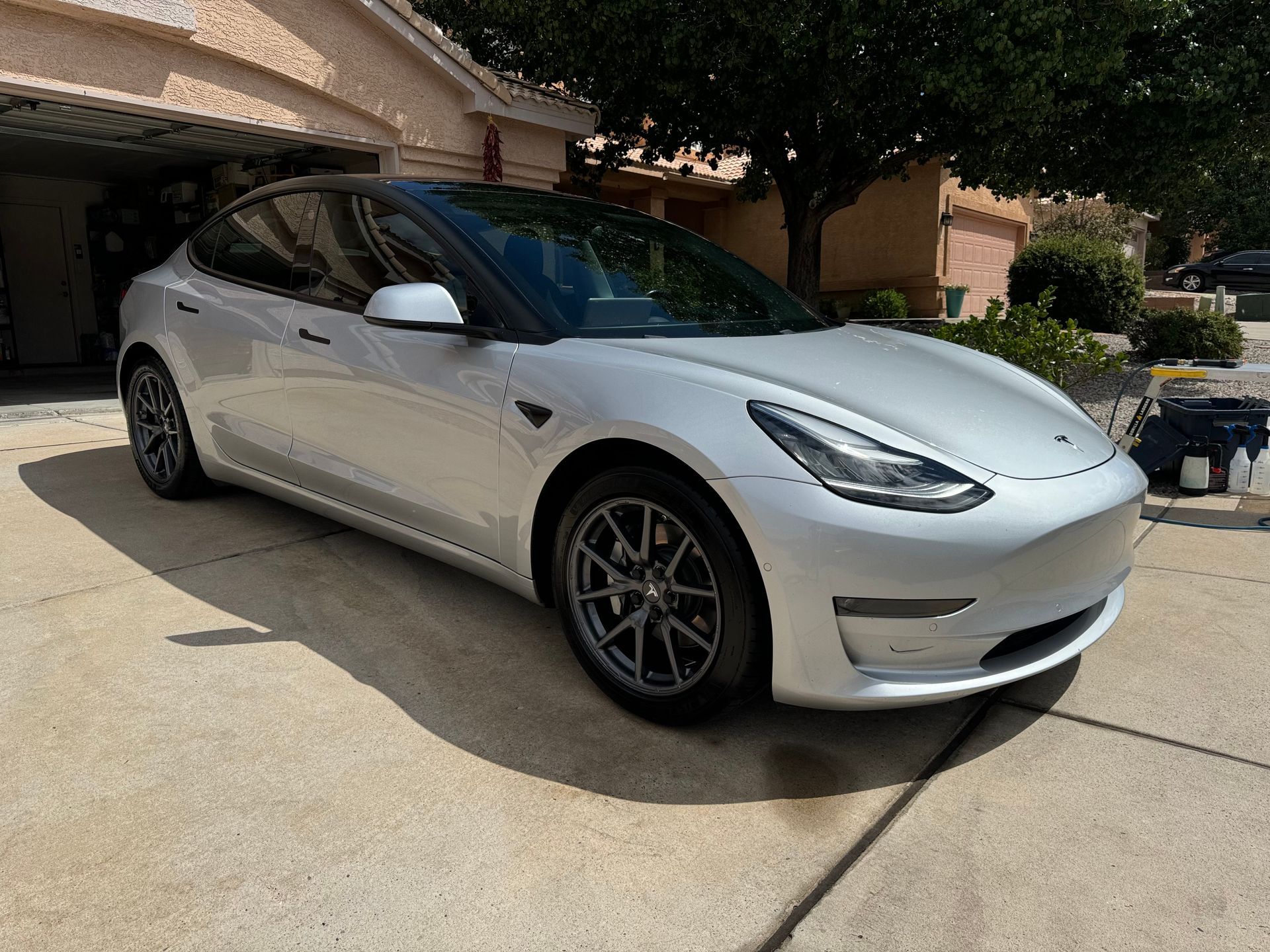 Silver Tesla Model 3 parked on a driveway in front of a house.