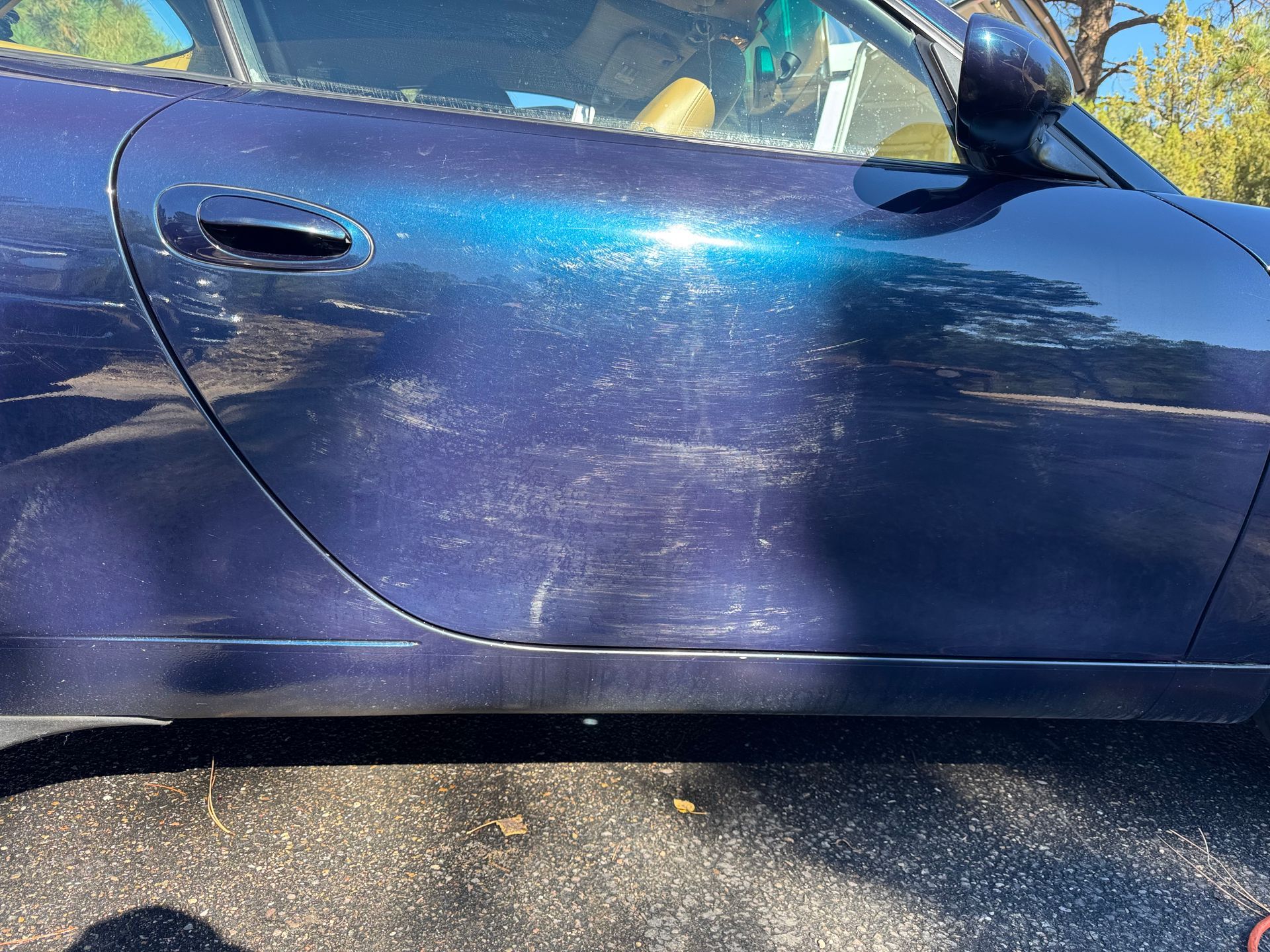Black car's rear, shiny after wash, with tail light and reflections in sunlight.