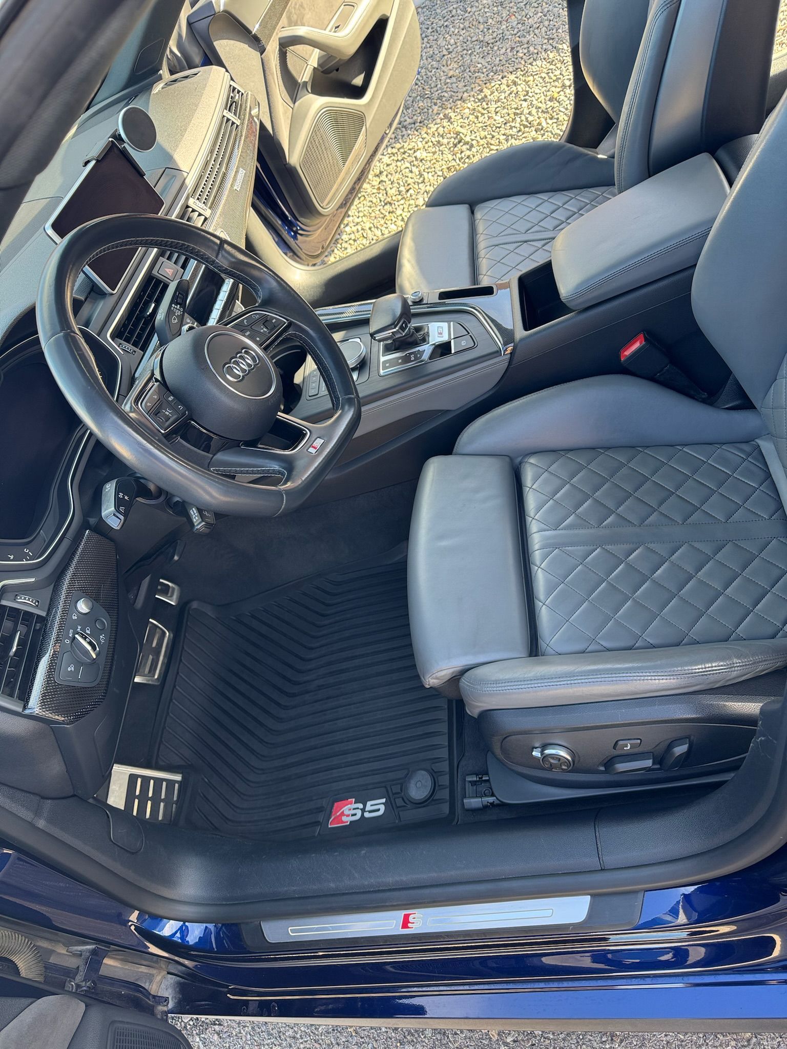 Blue Audi interior, black steering wheel, grey leather seats, black floor mats.