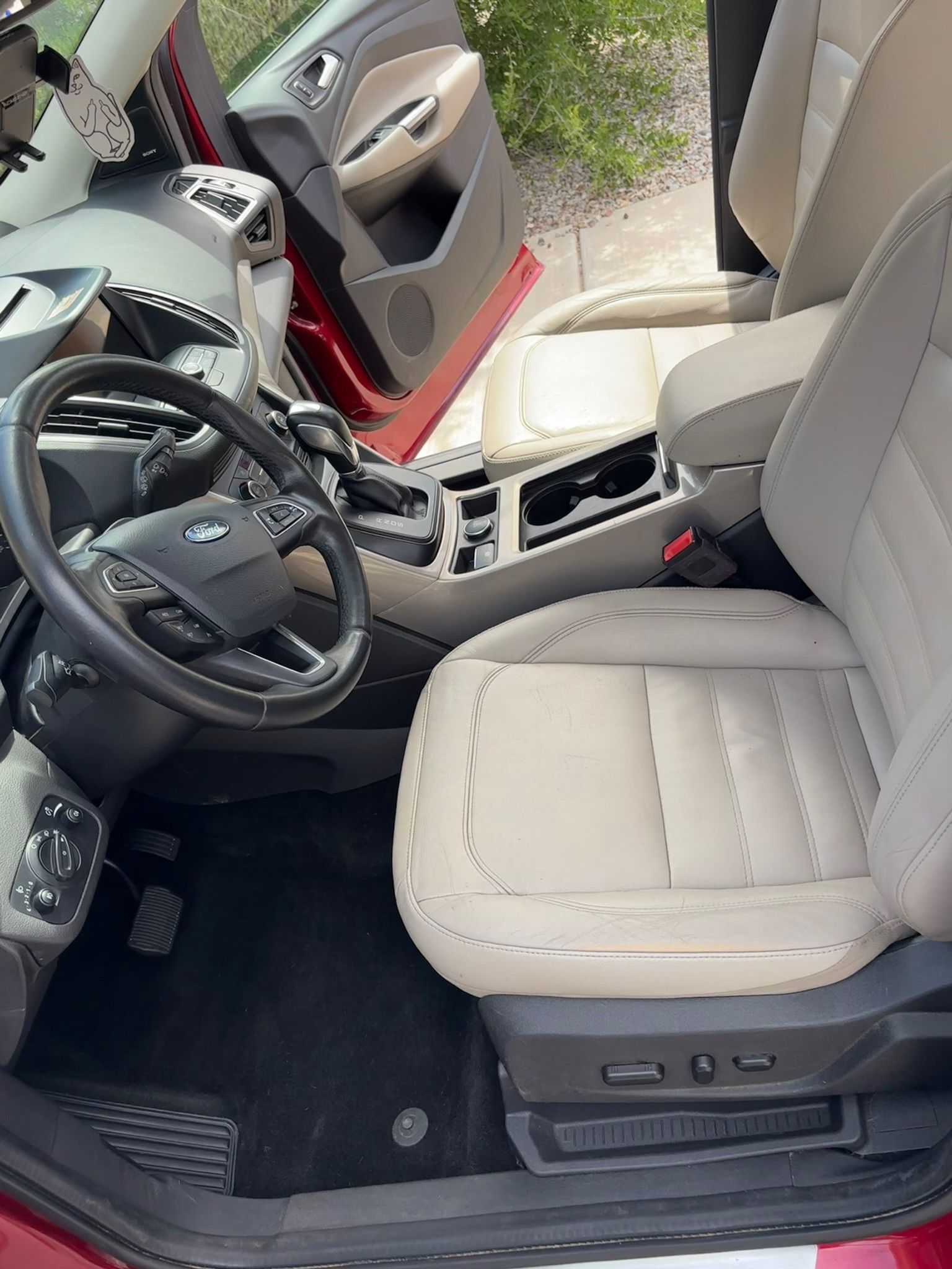 Interior of a red Ford Escape with tan leather seats, black steering wheel, and open door.