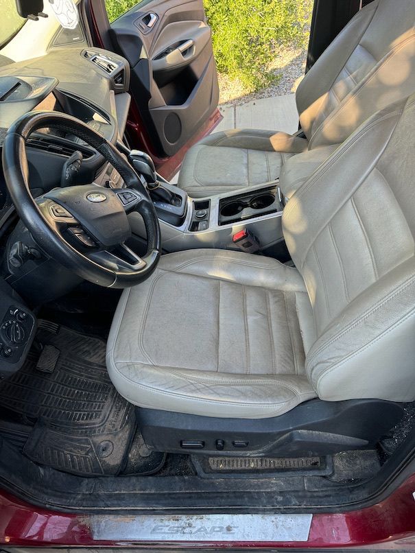 Interior of a Ford Escape. Tan leather seats, black steering wheel, and dirty floor mats.