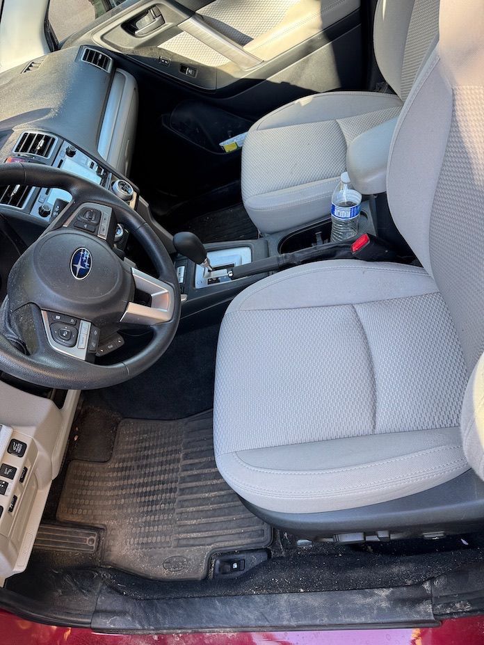 Interior of a Subaru Forester. Gray cloth seats, black floor mats, steering wheel and dashboard.