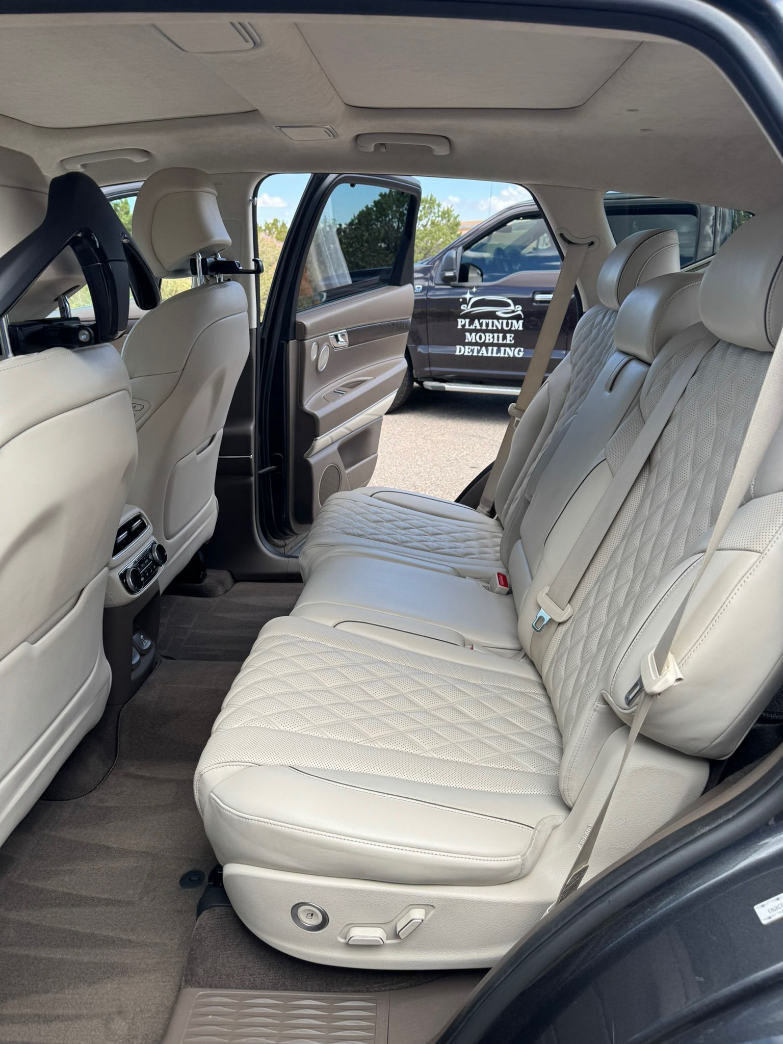 Beige quilted leather seats in the back of a dark SUV, door open.