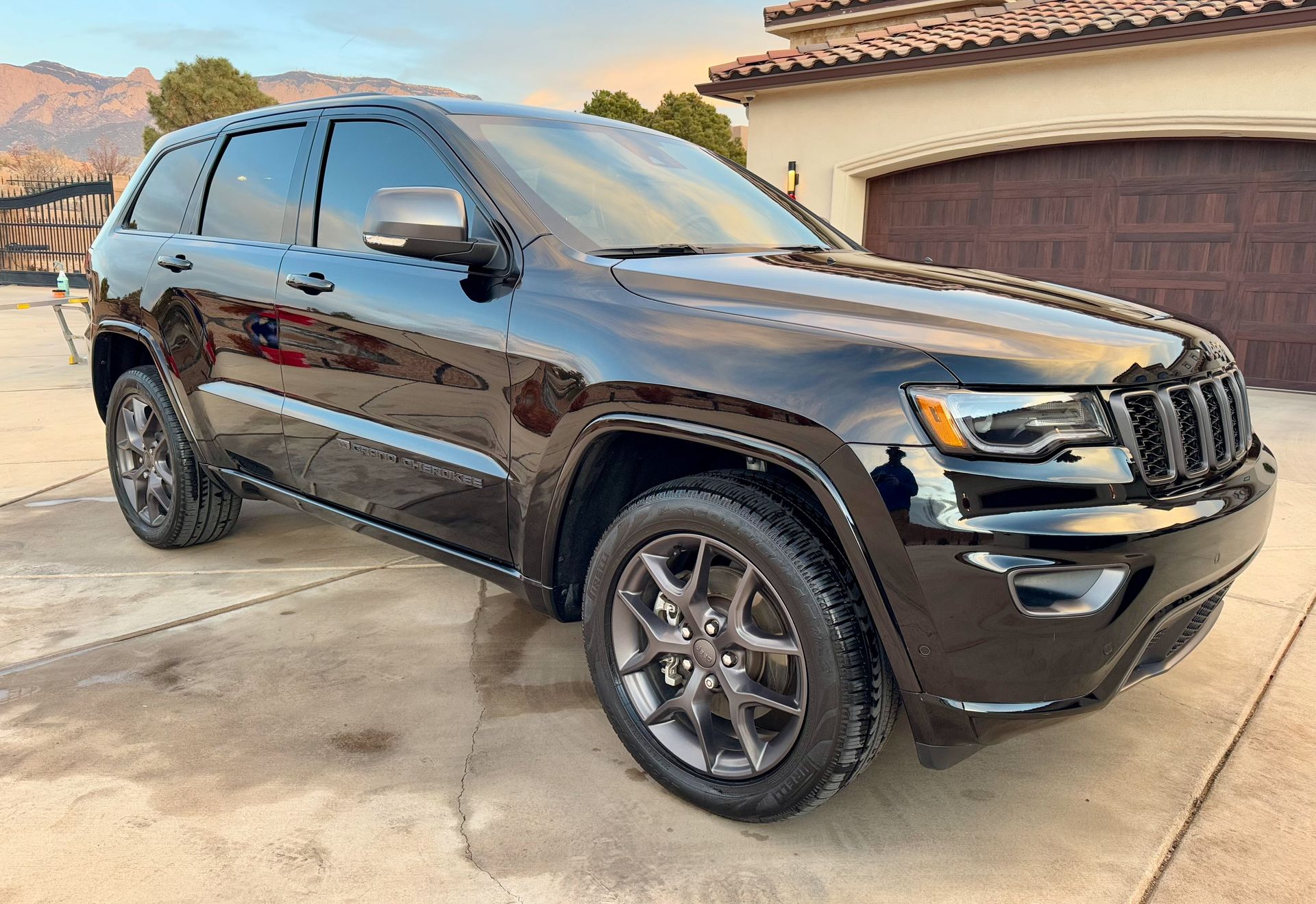 Black Jeep Grand Cherokee parked on a concrete driveway, with a house and mountain backdrop.