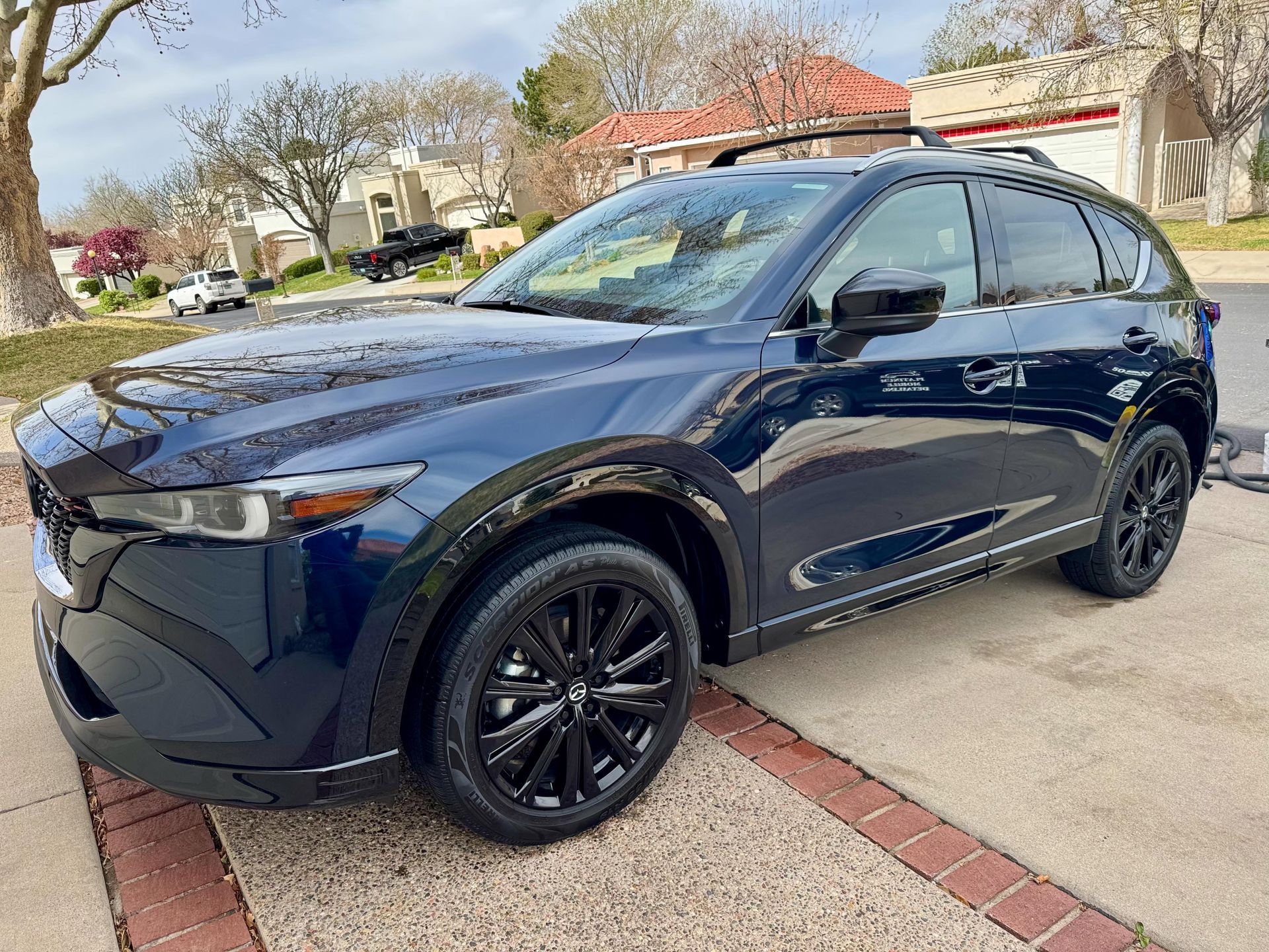 Dark blue Mazda CX-5 SUV parked on a driveway; black wheels and roof rack; suburban setting.
