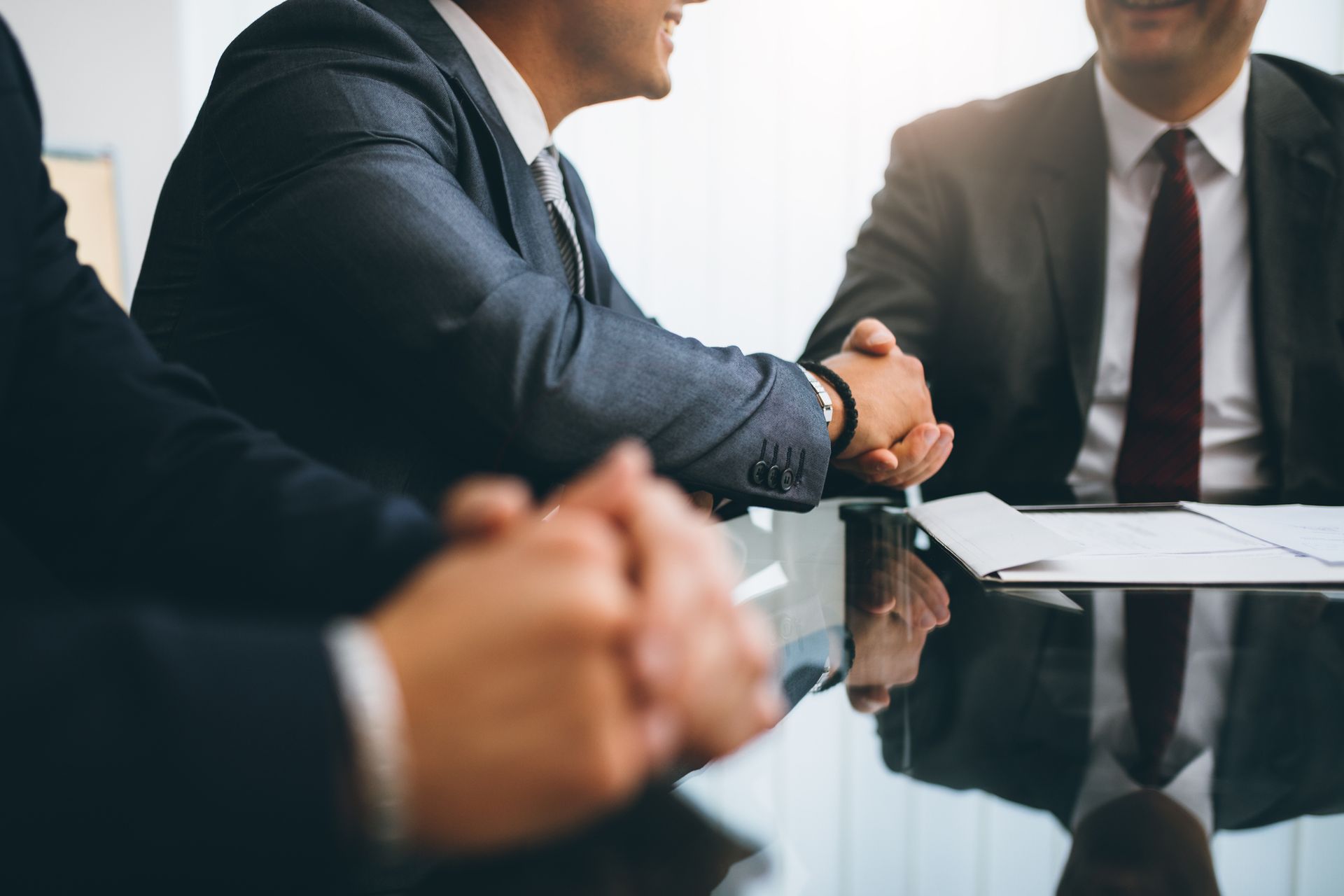 A group of businessmen are sitting at a table shaking hands.
