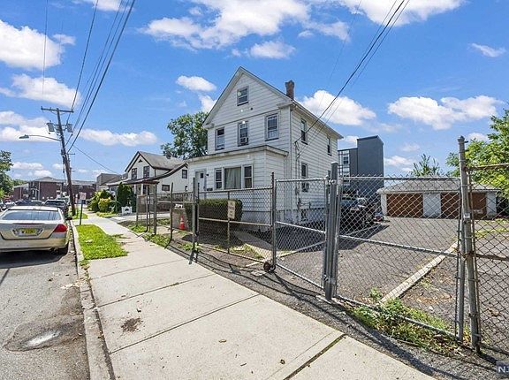 A white car is parked on the sidewalk in front of a white house.