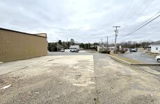 A parking lot with a building in the background and a street in the foreground.