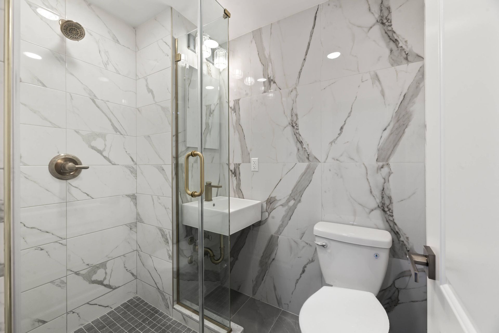 A bathroom with a toilet , sink , shower and marble walls.