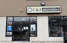 The front of a c & j electronics store with a car parked in front of it.