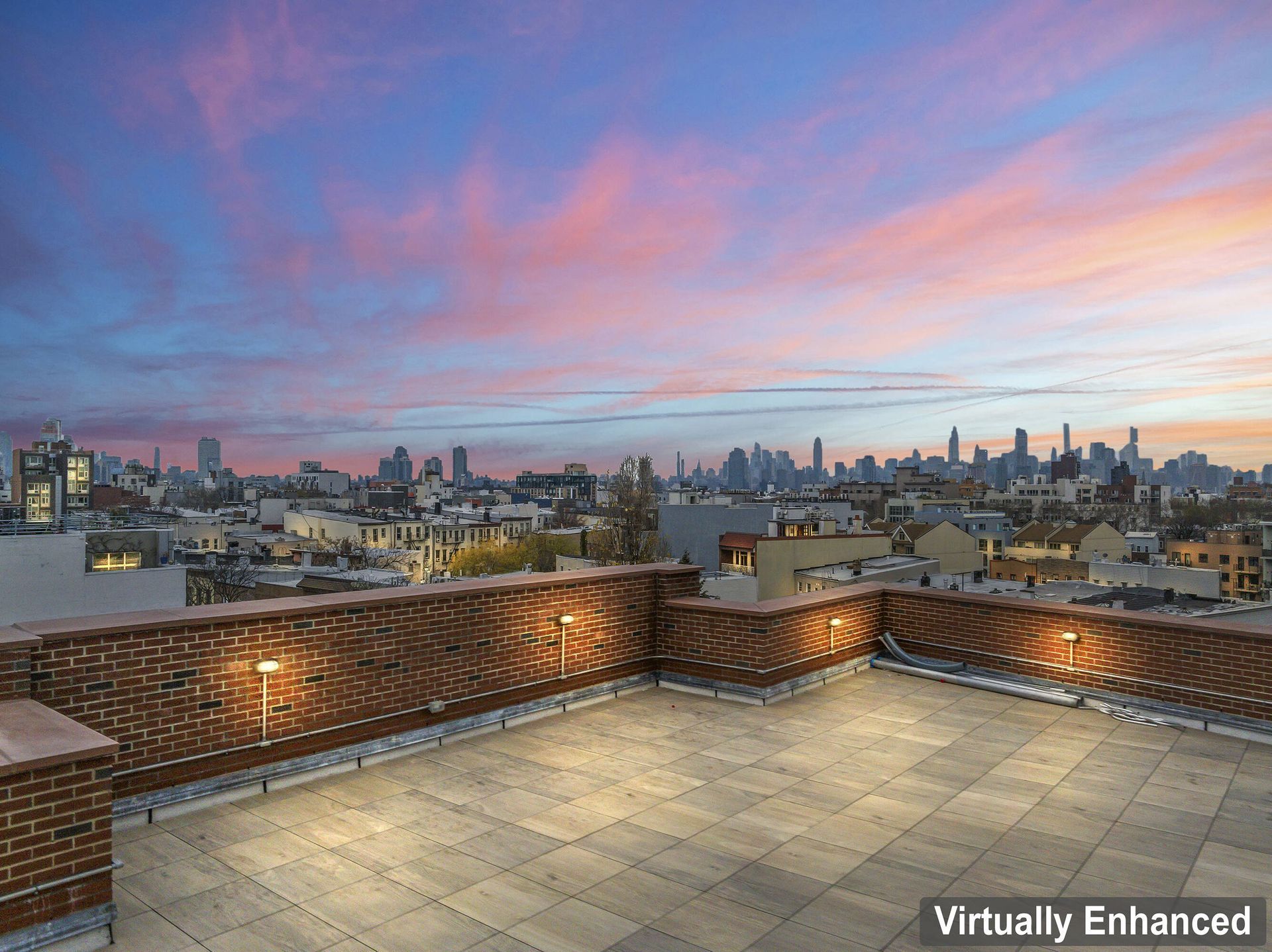 A rooftop terrace with a view of the city skyline at sunset.