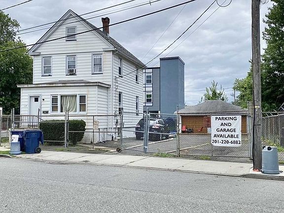A white house is behind a fence with a sign that says parking and garage available.