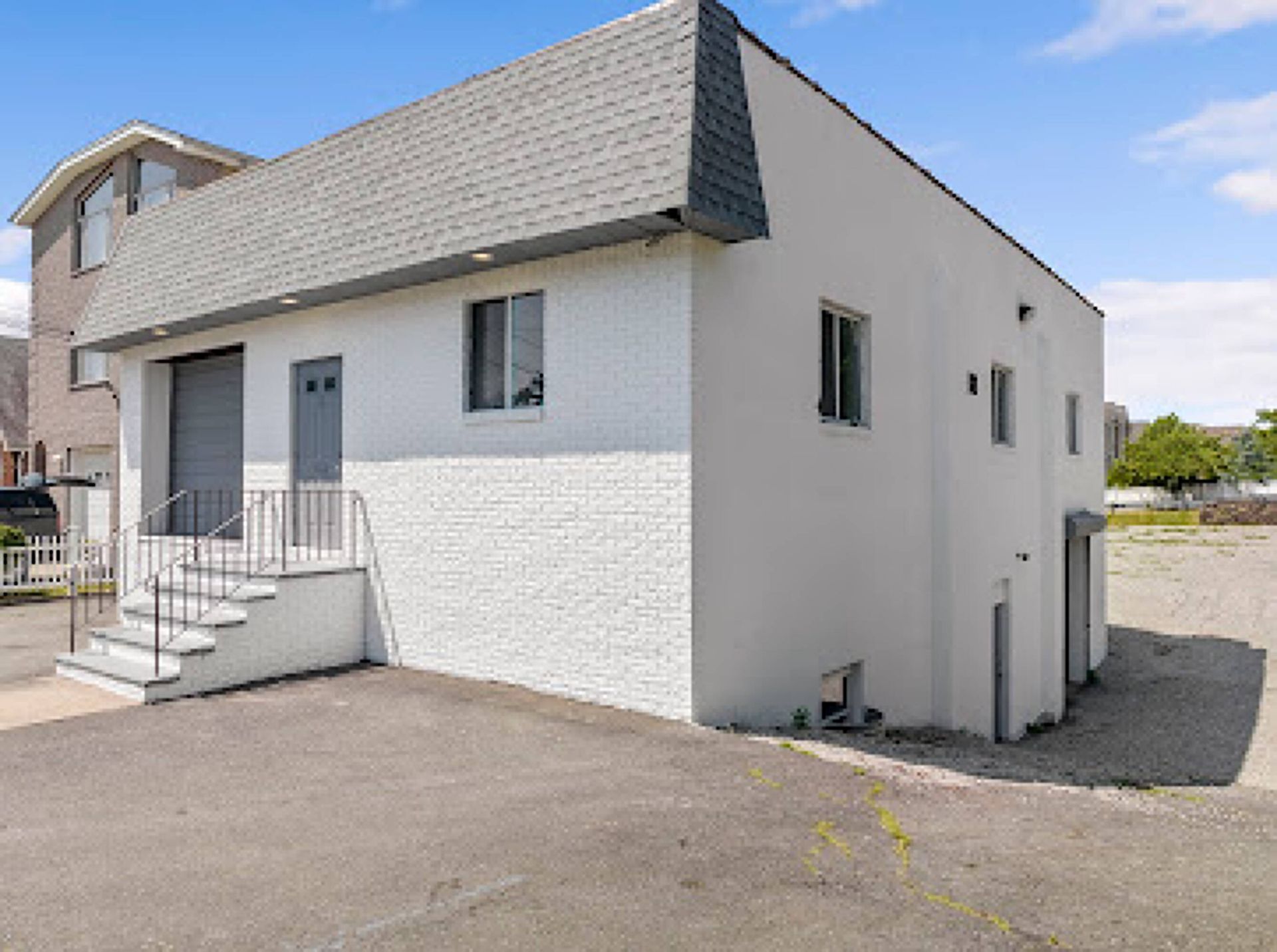 A white brick house with a gray garage door and stairs leading up to it.