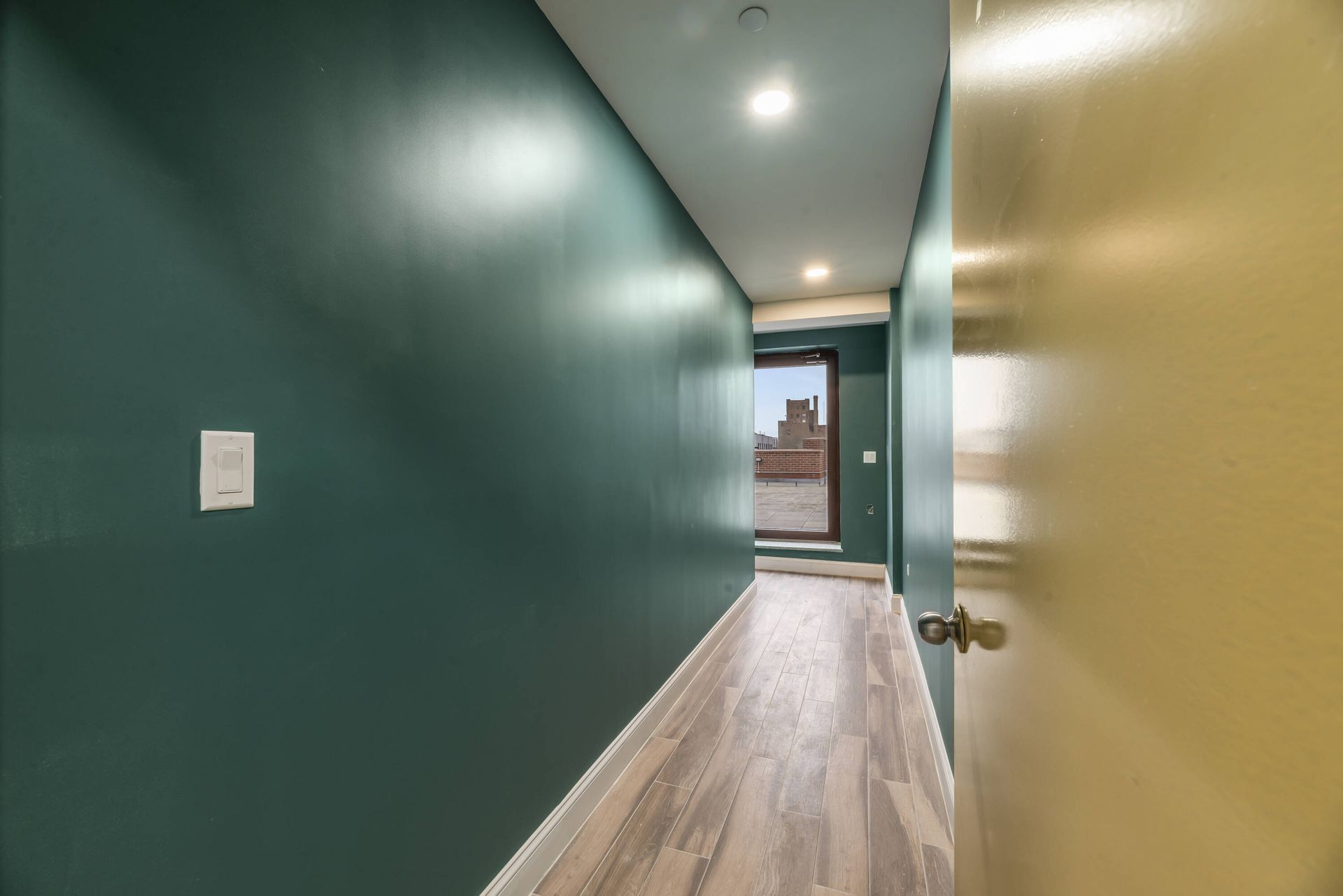 A long hallway with green walls and wooden floors leading to a door.