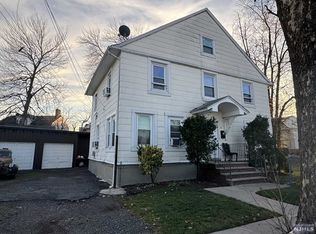 A white house with a garage and a tree in front of it.