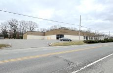 A car is parked in front of a large building next to a road.