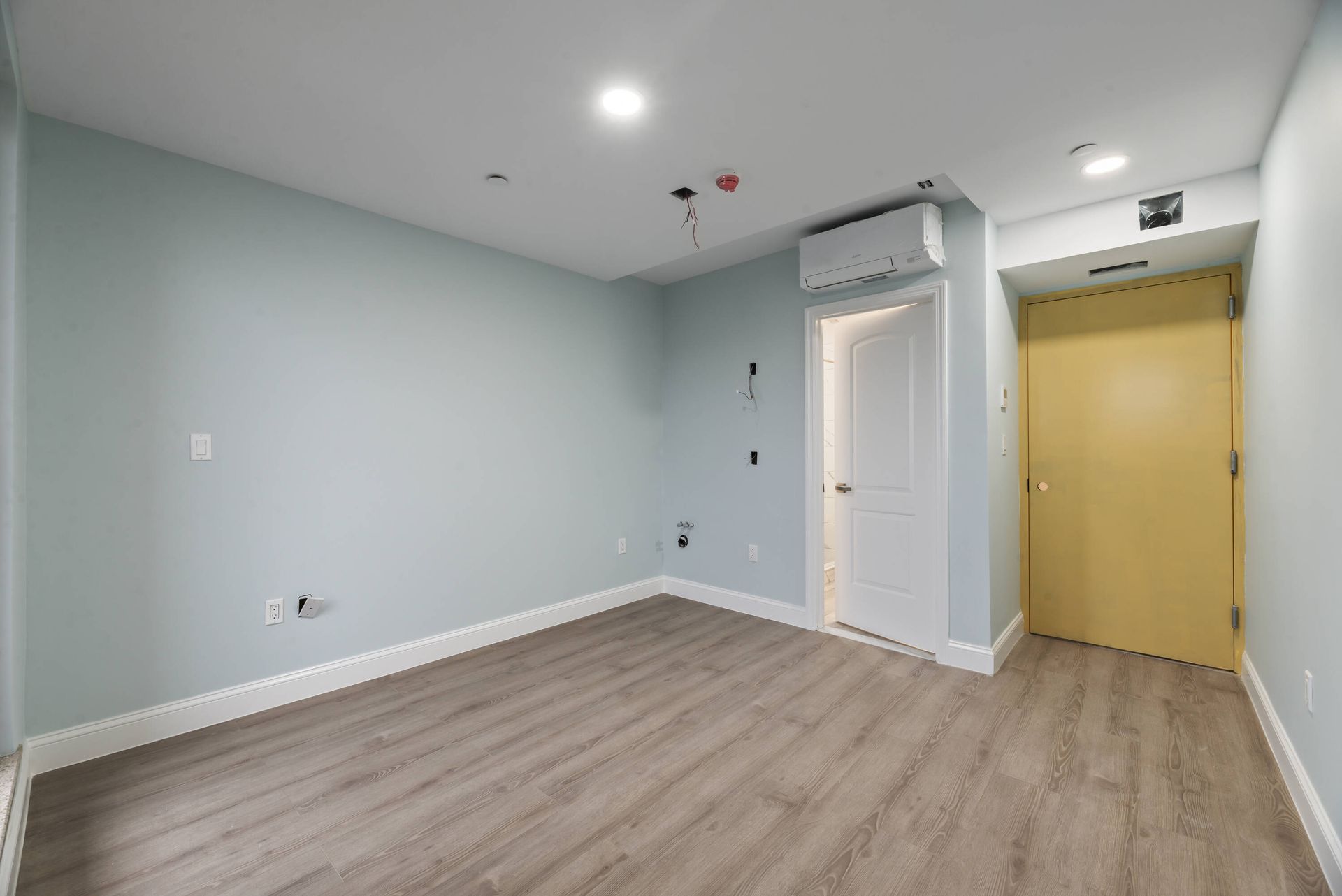 An empty room with hardwood floors and a yellow door.