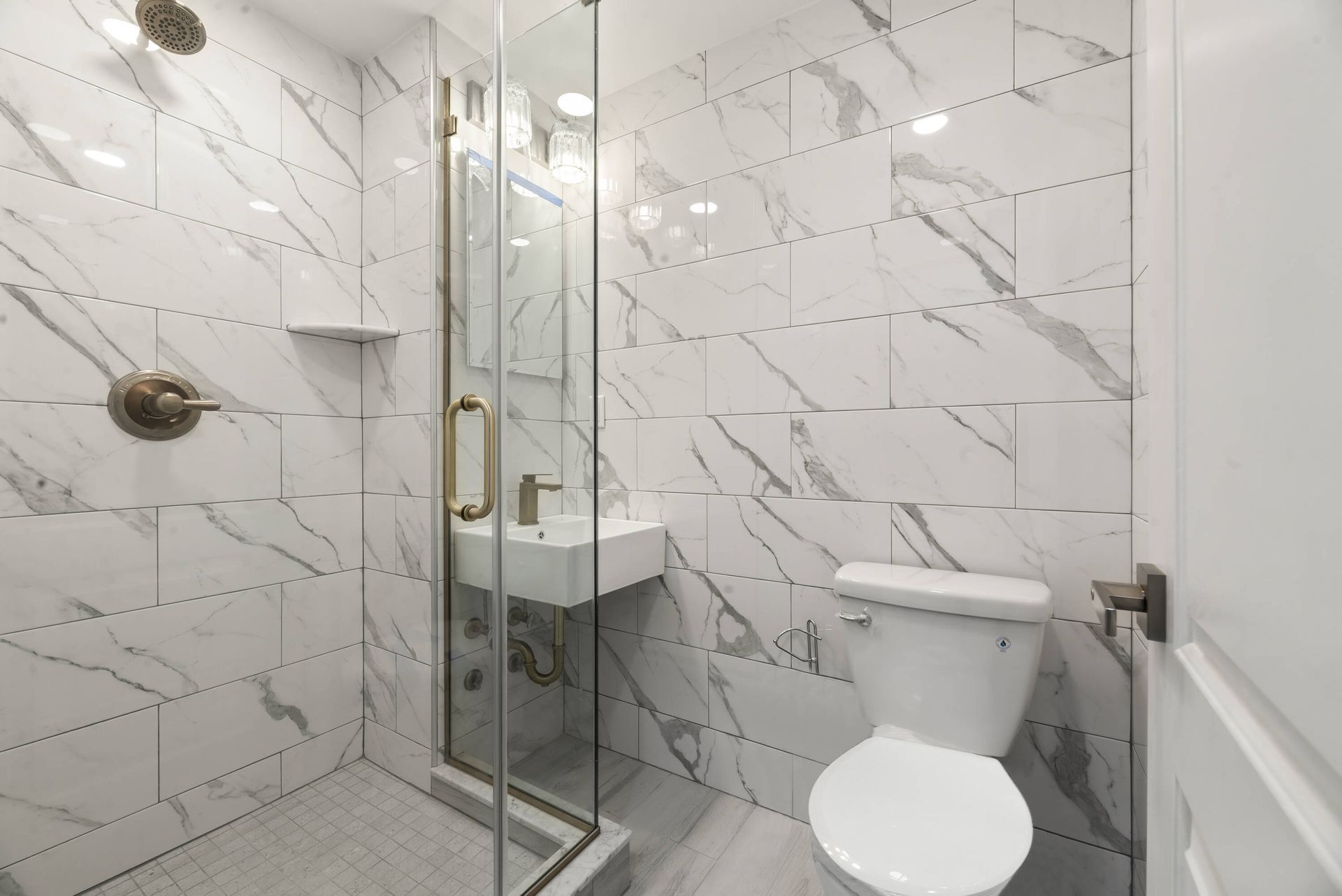 A bathroom with marble tiles , a toilet , sink and shower.