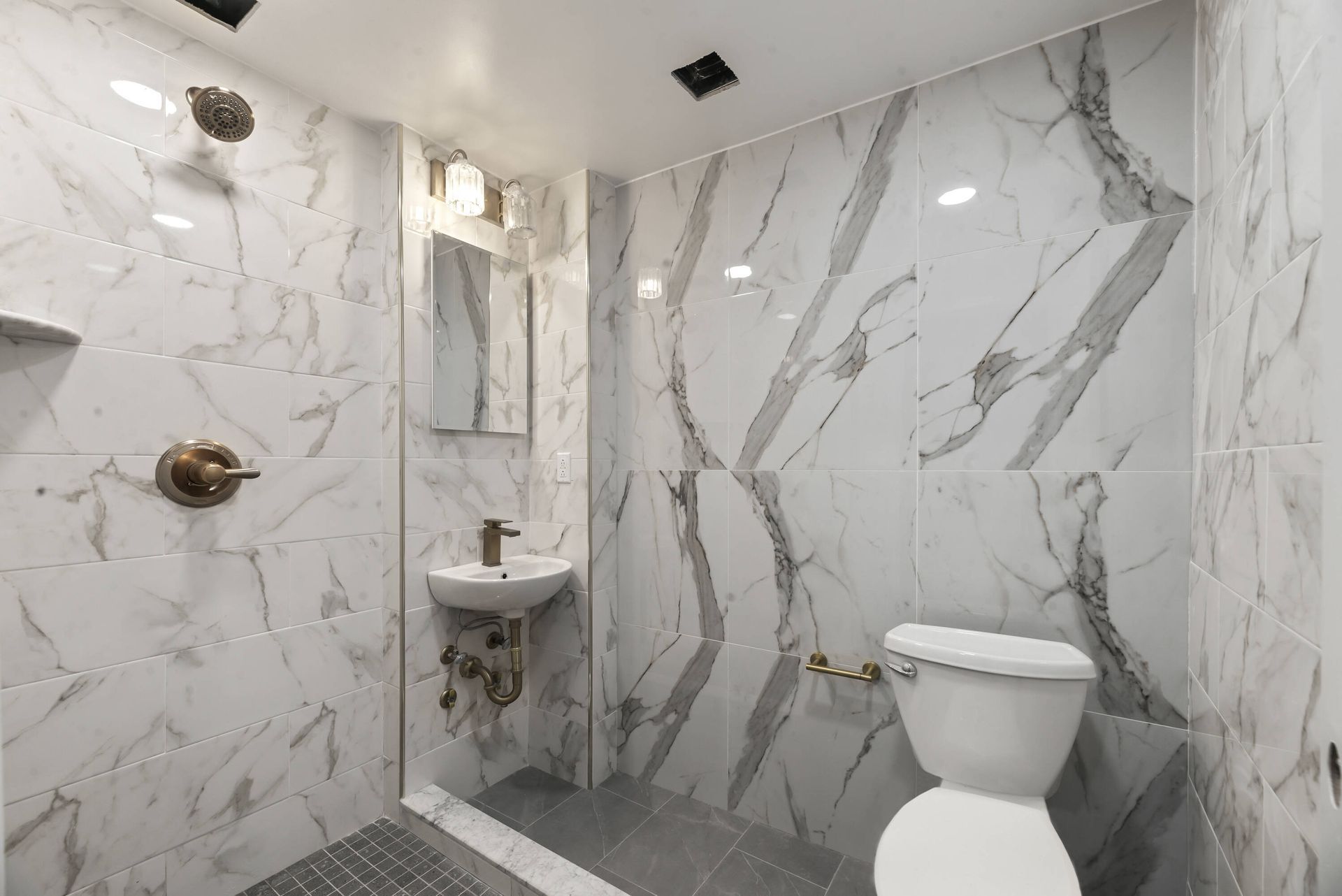 A bathroom with marble walls , a toilet , sink and shower.