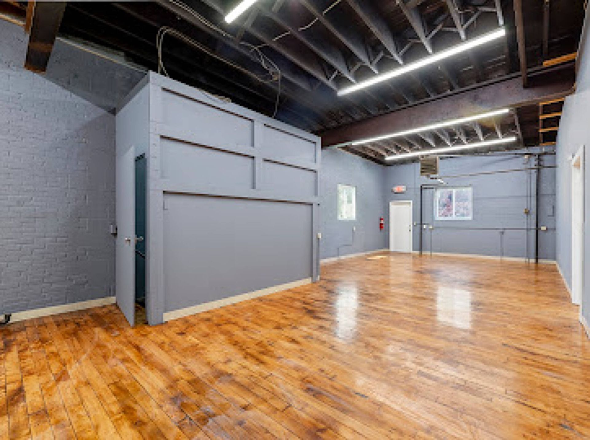 A large empty room with wooden floors and a gray wall.