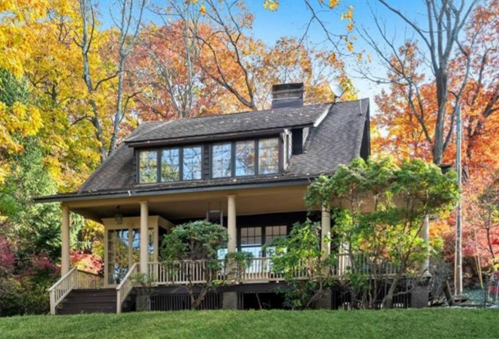A small house with a large porch is surrounded by trees in the woods.