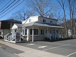 A small white house with a parking lot in front of it.