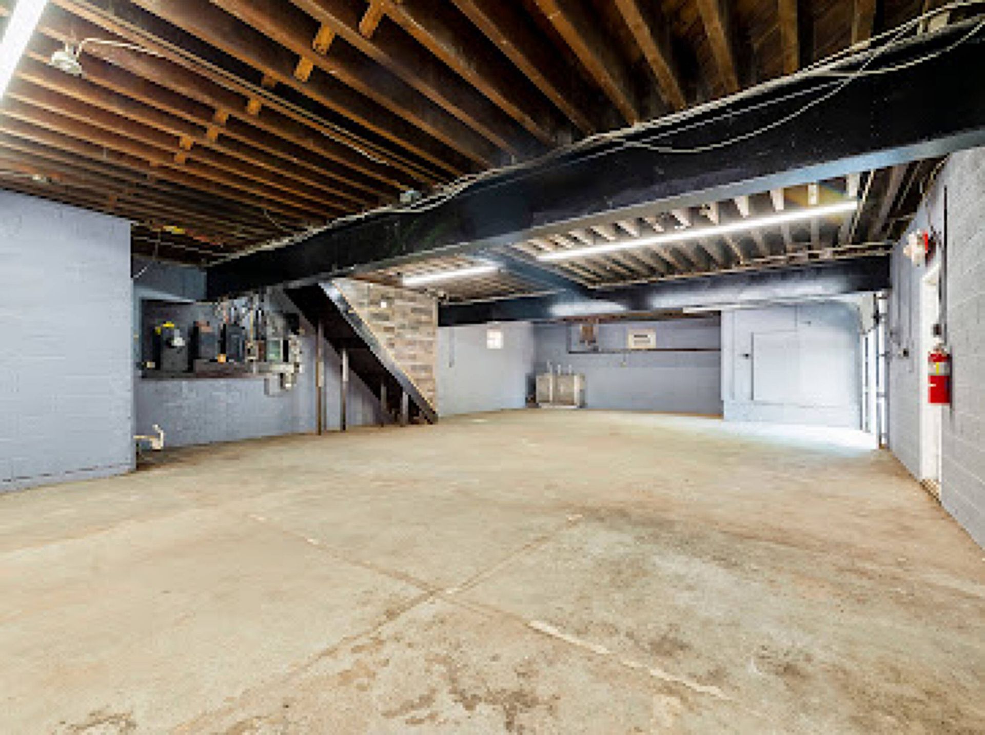 An empty basement with a wooden ceiling and stairs.