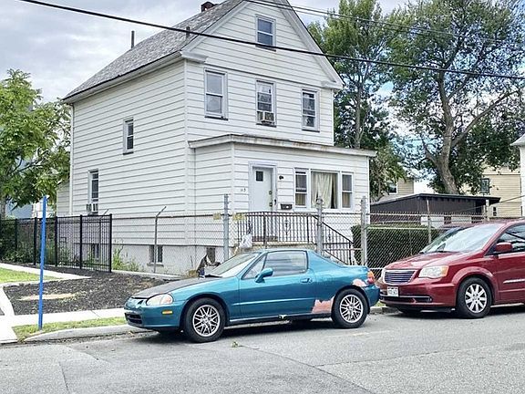 A blue car is parked in front of a white house.