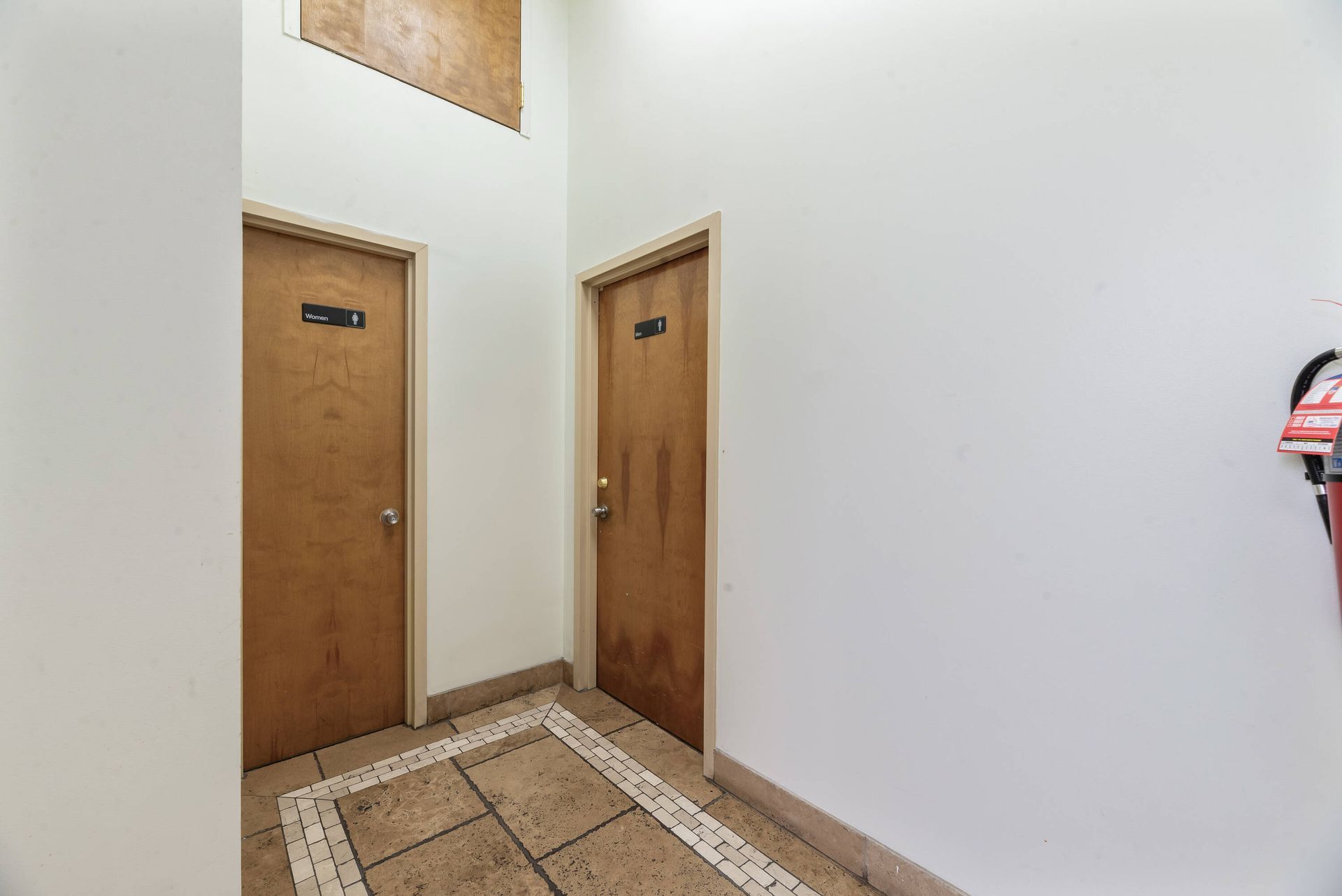 A hallway with two wooden doors and a fire extinguisher on the wall.